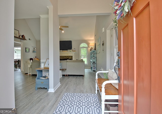 foyer featuring high vaulted ceiling, ceiling fan, a fireplace, and wood finished floors