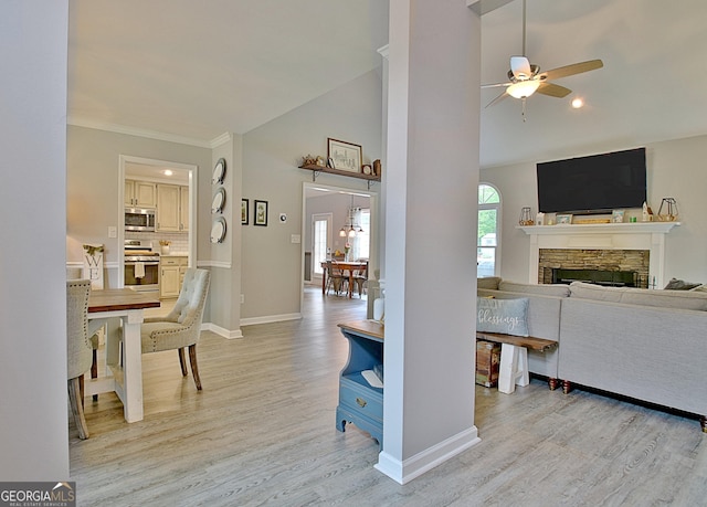 living room featuring lofted ceiling, light wood-style floors, baseboards, a stone fireplace, and a ceiling fan