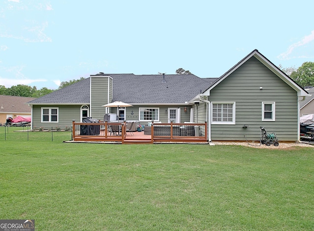 back of house featuring a lawn, a deck, a chimney, and roof with shingles