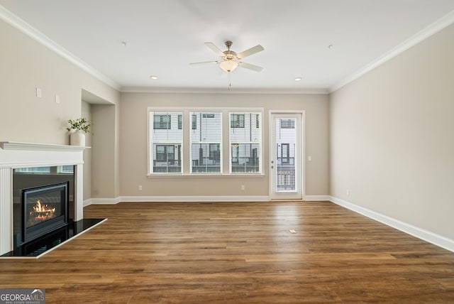 unfurnished living room featuring ornamental molding, a glass covered fireplace, wood finished floors, baseboards, and ceiling fan