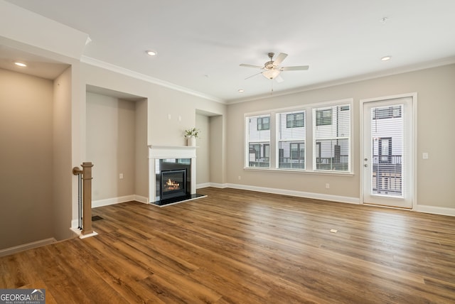 unfurnished living room with a ceiling fan, crown molding, wood finished floors, a glass covered fireplace, and recessed lighting
