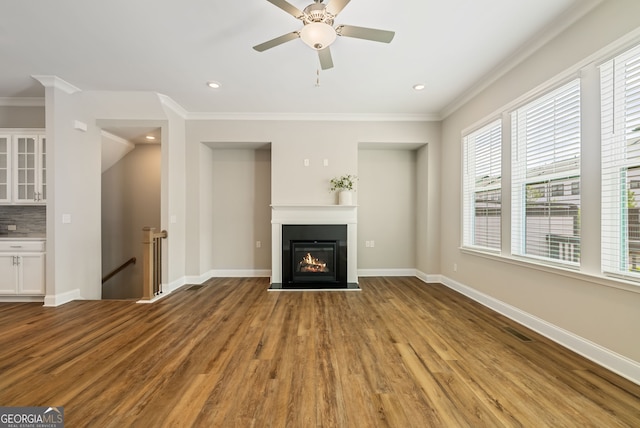 unfurnished living room featuring ceiling fan, a glass covered fireplace, wood finished floors, visible vents, and ornamental molding