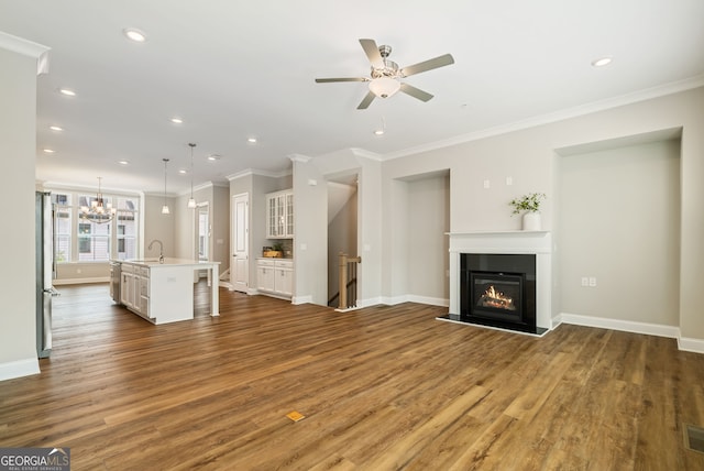 unfurnished living room with crown molding, wood finished floors, a sink, ceiling fan with notable chandelier, and a glass covered fireplace