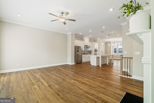 unfurnished living room featuring recessed lighting, ornamental molding, ceiling fan with notable chandelier, and wood finished floors