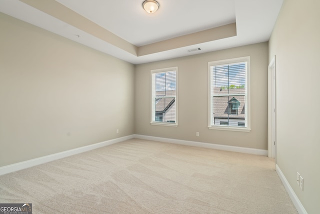 unfurnished room featuring baseboards, visible vents, light carpet, and a raised ceiling