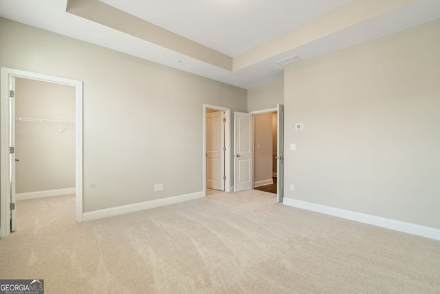 unfurnished bedroom with a walk in closet, baseboards, carpet, and a tray ceiling