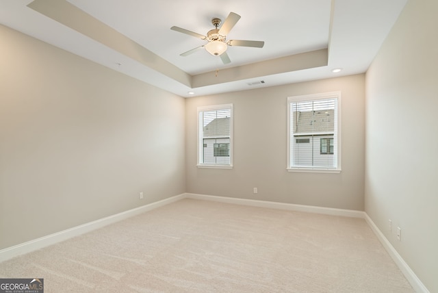 spare room with light colored carpet, baseboards, visible vents, and a tray ceiling