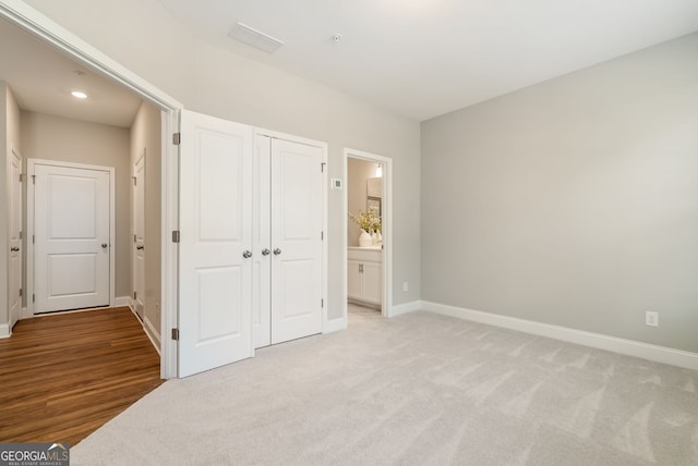 unfurnished bedroom featuring baseboards, light carpet, a closet, and ensuite bath
