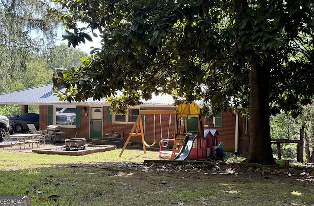 rear view of property featuring a lawn, brick siding, a fire pit, and a playground