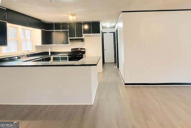 kitchen featuring a peninsula, dark countertops, light wood-type flooring, black range with electric stovetop, and a sink