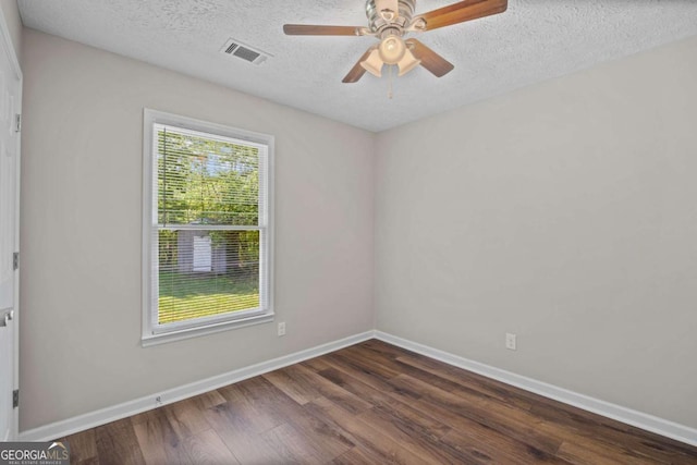empty room featuring a textured ceiling, dark wood finished floors, a ceiling fan, baseboards, and visible vents