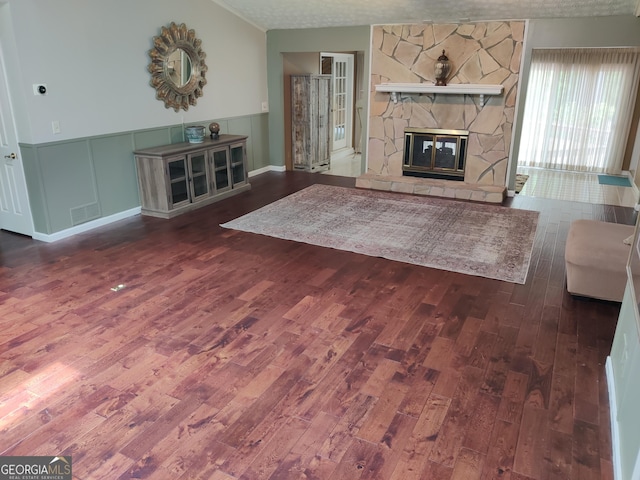 living room featuring a stone fireplace, visible vents, wainscoting, and wood finished floors