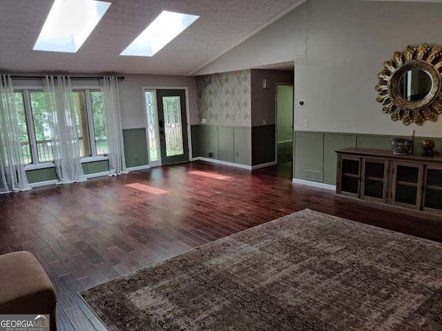unfurnished living room with vaulted ceiling with skylight, wainscoting, and wood finished floors