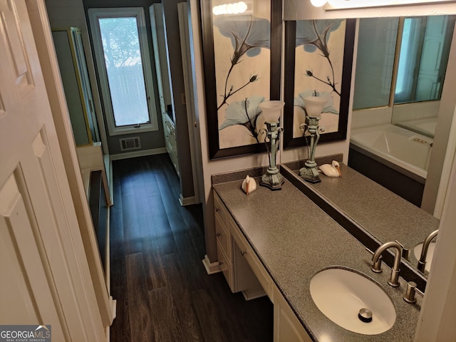 bathroom featuring visible vents, vanity, wood finished floors, baseboards, and a tub