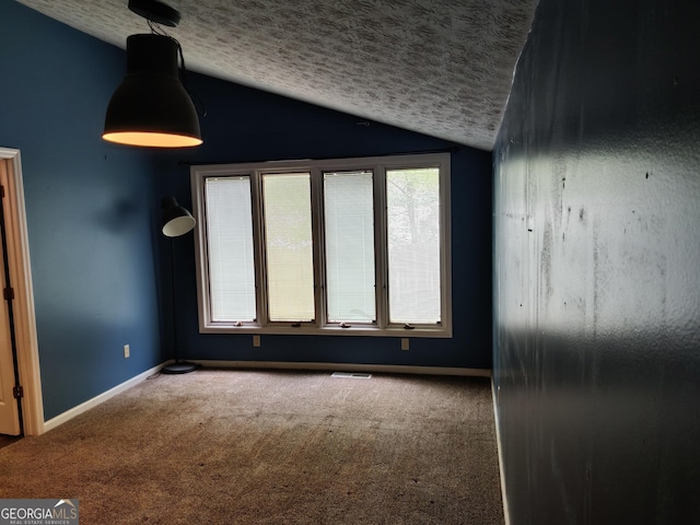 carpeted empty room featuring a textured ceiling, vaulted ceiling, baseboards, and visible vents