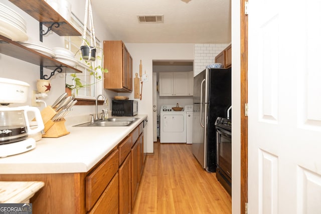 kitchen with independent washer and dryer, visible vents, a sink, black appliances, and light wood-style floors