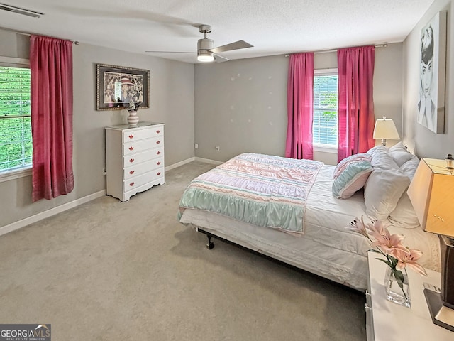 carpeted bedroom with a textured ceiling, baseboards, visible vents, and a ceiling fan