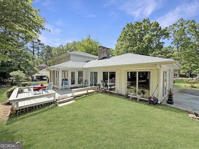 back of property featuring a lawn, a shingled roof, a wooden deck, and a chimney