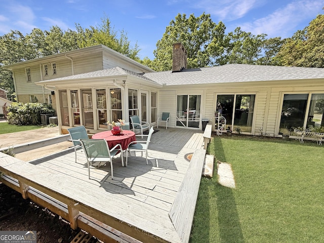 back of house featuring roof with shingles, a sunroom, a deck, a chimney, and a lawn