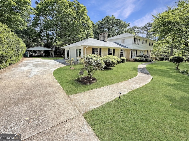 view of front of home with brick siding, a front yard, a chimney, a carport, and driveway