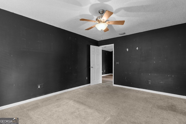 carpeted empty room featuring a textured ceiling, ceiling fan, visible vents, and baseboards