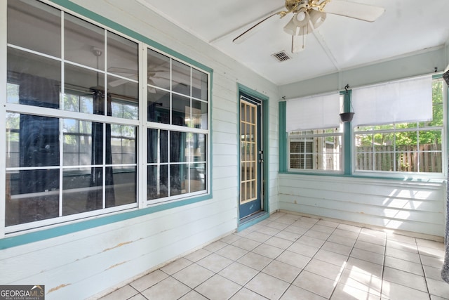 unfurnished sunroom with visible vents, ceiling fan, tile patterned floors, and wooden walls