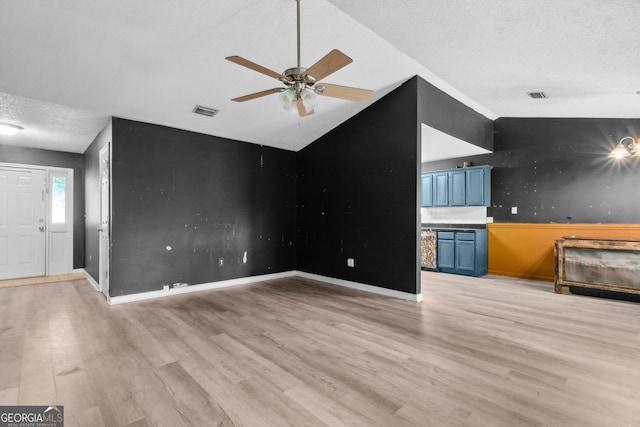 unfurnished living room featuring a textured ceiling, a ceiling fan, lofted ceiling, light wood-type flooring, and visible vents