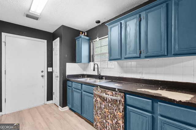 kitchen featuring stainless steel dishwasher, dark countertops, a sink, and blue cabinets