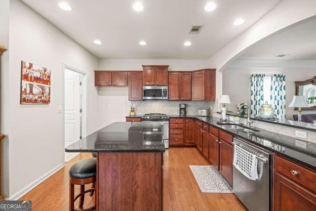 6408 Autumn Crest Ln, Hoschton, GA 30548 - kitchen with appliances with stainless steel finishes, a sink, arched walkways, dark stone counters, and light wood-style flooring