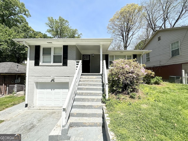 split level home featuring brick siding, a garage, central AC unit, covered porch, and driveway