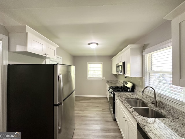 kitchen with a sink, white cabinets, light stone countertops, and stainless steel appliances