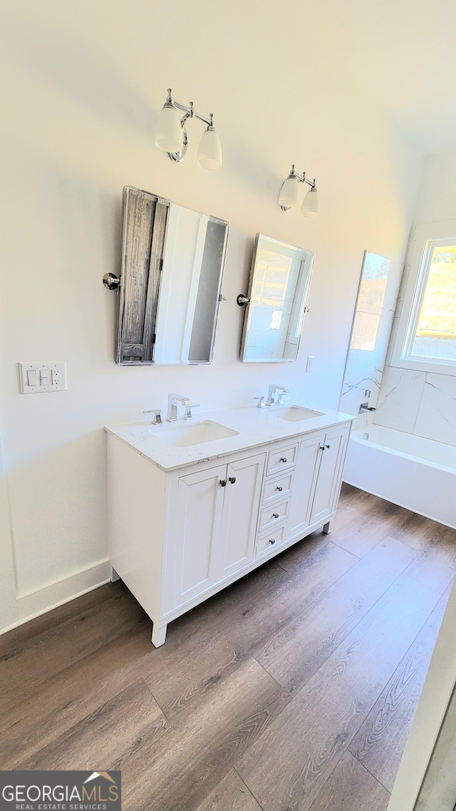 bathroom featuring a sink, a bathing tub, double vanity, and wood finished floors
