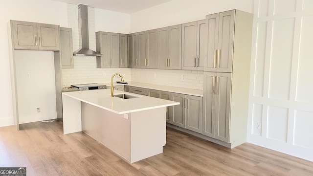 kitchen with wall chimney range hood, gray cabinets, decorative backsplash, and a sink
