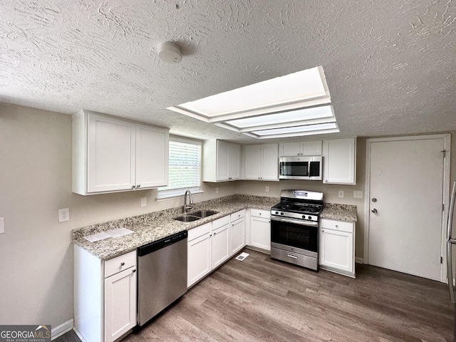 kitchen with white cabinets, appliances with stainless steel finishes, a sink, a textured ceiling, and dark wood finished floors