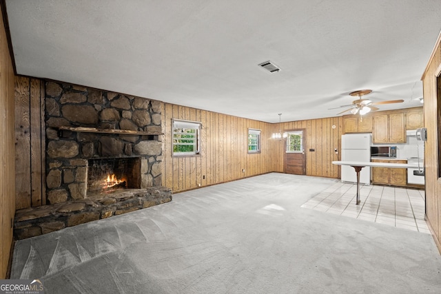 unfurnished living room featuring visible vents, wood walls, a fireplace, light colored carpet, and a ceiling fan
