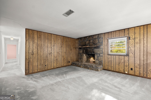 unfurnished living room featuring carpet floors, wood walls, a stone fireplace, and visible vents