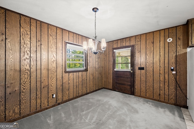 unfurnished dining area featuring carpet floors, wooden walls, a notable chandelier, and a healthy amount of sunlight