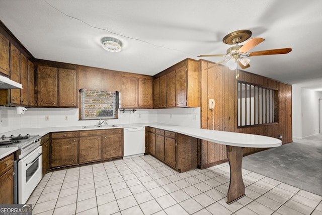 kitchen featuring a ceiling fan, a sink, light countertops, wooden walls, and white appliances