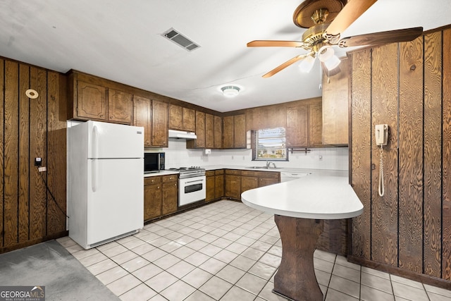 kitchen with visible vents, a sink, a peninsula, under cabinet range hood, and white appliances