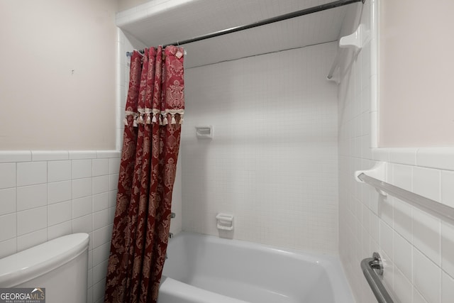 bathroom with toilet, tile walls, wainscoting, and shower / tub combo