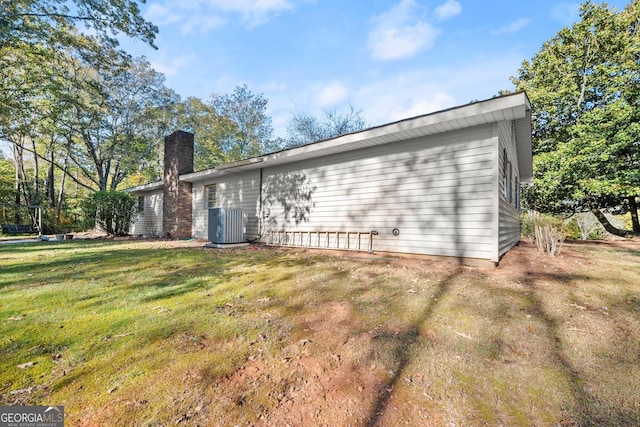 back of house with central AC unit, a chimney, and a yard