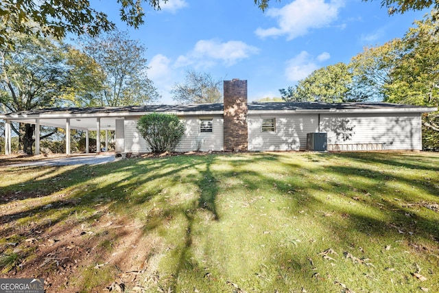 back of house with a lawn, a carport, a chimney, and cooling unit