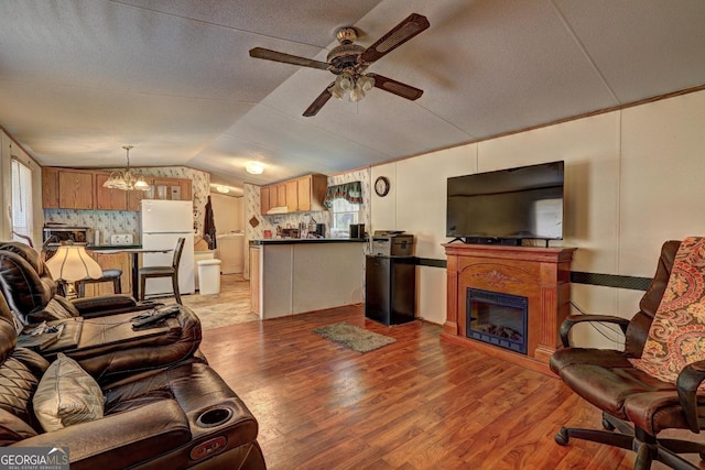 living area with a glass covered fireplace, light wood-type flooring, a textured ceiling, ceiling fan with notable chandelier, and vaulted ceiling