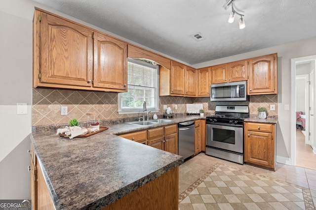kitchen featuring visible vents, a peninsula, dark countertops, a sink, and appliances with stainless steel finishes