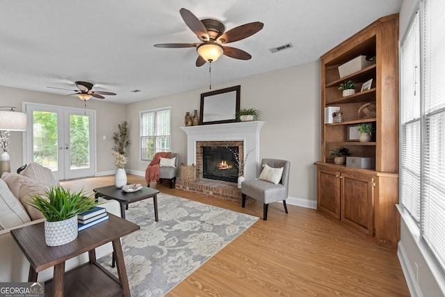 living room with ceiling fan, visible vents, a fireplace, light wood-type flooring, and baseboards