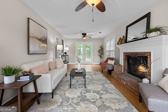 living area featuring baseboards, ceiling fan, a fireplace, and wood finished floors