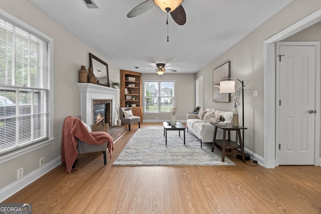 living area with visible vents, a glass covered fireplace, light wood-style floors, baseboards, and ceiling fan