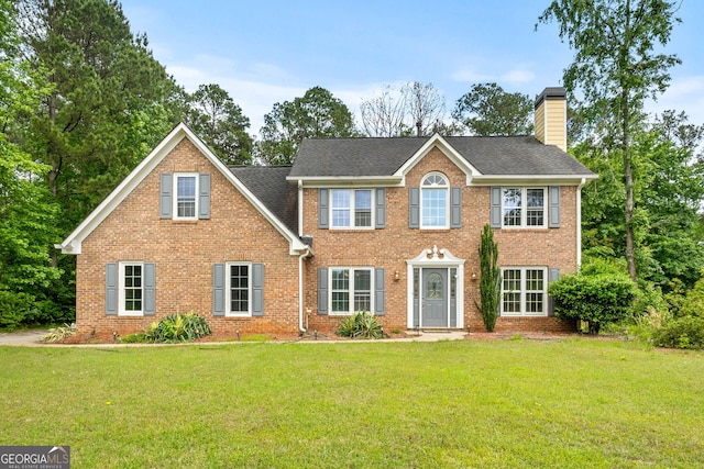 colonial house with brick siding, a chimney, a front yard, and roof with shingles
