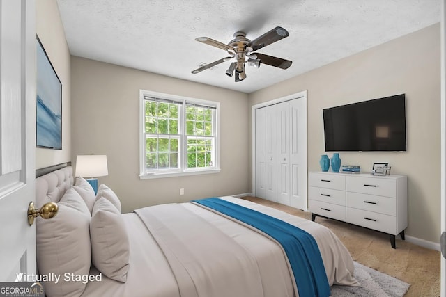 bedroom with a ceiling fan, a textured ceiling, light colored carpet, baseboards, and a closet