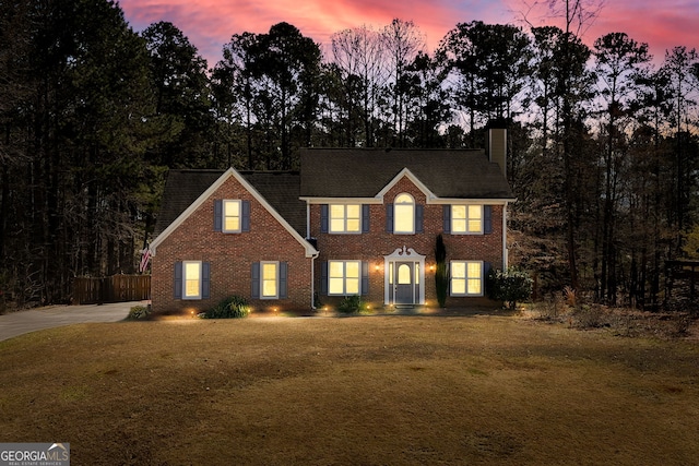 colonial home with a chimney, a front lawn, and brick siding